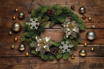 Christmas wreath with cones, baubles and decorative snowflakes on wooden table, flat lay