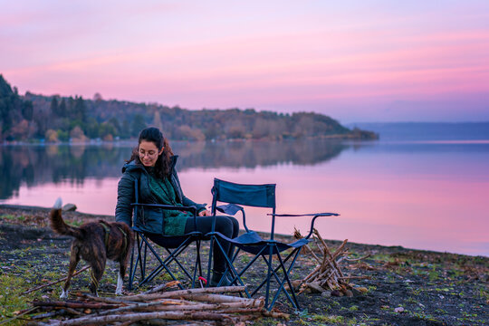 Woman playing with a dog with a wooden stick near a lake at sunset