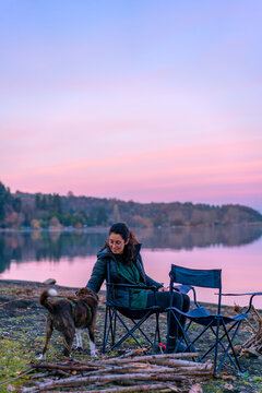 Woman playing with a dog with a wooden stick near a lake at sunset