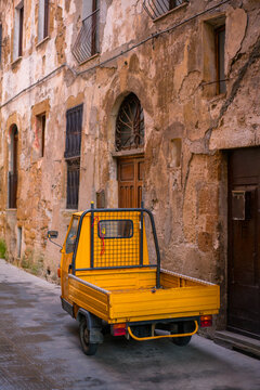 Iconic yellow Ape three wheeler on an antique street of Italy