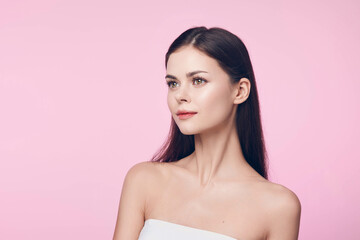 Beautiful young woman with long dark hair and white dress posing on a pink background with copy space