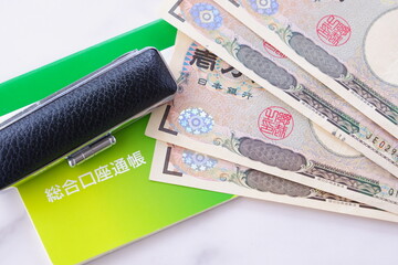 テーブルの上に置かれた銀行の預金通帳と印鑑、1万円札
