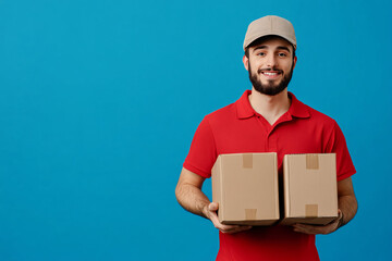 A happy courier wearing a red shirt and cap holds two cardboard boxes, standing against a bright blue background, ready for delivery