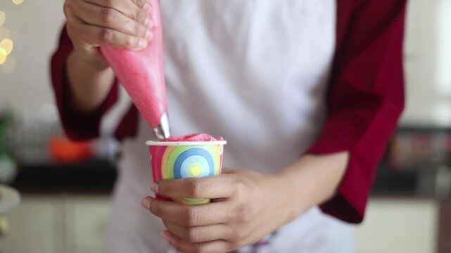 Indian Woman Squeezing pink icing  on cupcake closeup.  christmas preparation, Bakery Food and dessert,  Closeup of hand. 