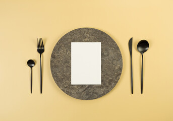 Top view of brown marble plate, black cutlery and white card on yellow background. Food...