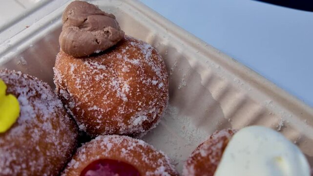 Close up view of various flavored malasadas. Malasada fried Portuguese donuts sprinkled with sugar. Closeup of sweet delicious malasada donut held in a takeout container. Malasadas, hawaiian
