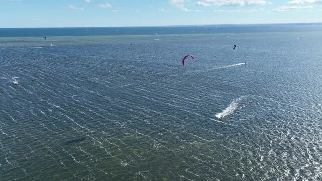 People swim in the sea on a kiteboard or kitesurfing. Summer sport learning how to kitesurf. Kite surfing on Puck bay in Jastarnia, Poland, Europe aerial drone video view. Kitesurfing at the sea bay.