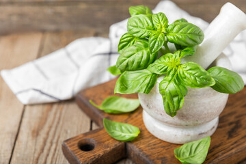 Fresh green basil in a mortar on a textured wooden background. Organic spices and herbs. Vegan. Fresh kitchen herbs. Fresh basil being made into pesto with mortar and pestle.Copy space. Place for text