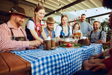 Two women, waitress dressed in Bavarian clothes serving beer to a group of friends meeting at pub...