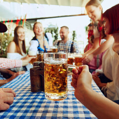Focus on lager beer mug and blurred people, friends sitting at table at bar and celebrating, drinking, talking. Concept of Oktoberfest, festival, party, brewery, traditions