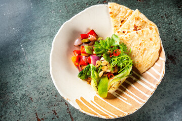 A vibrant plate of food featuring a side of flatbread, a colorful vegetable salad with mixed greens, and garnished with fresh herbs on a patterned ceramic plate against a dark background.