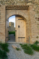 Obraz premium Wooden gate in a niche of stone and brick wall of Chailuri fortress. Gravel path, green grass