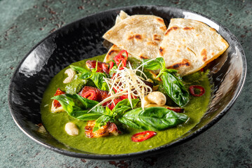 Fresh spinach soup with croutons, sun-dried tomatoes, and flatbread in a black bowl. Perfect for a healthy and delicious meal. Ideal for food photography, culinary blogs, and restaurant menus.