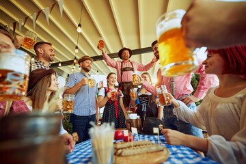 Men in traditional Bavarian clothes cheering group of his friends, people meeting at local pub for beer festival celebration. Concept of Oktoberfest, festival, party, brewery, traditions