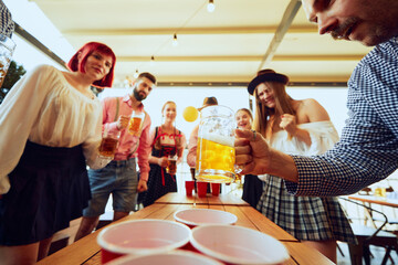 Focused and joyful faces, beer mugs in hand, Oktoberfest beer pong brings out competitive spirit, with fun and excitement in every throw. Concept of Oktoberfest, festival, party, brewery, traditions