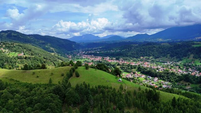 Flying over a grassy hill in the countryside revealing a village in a valley in Romania