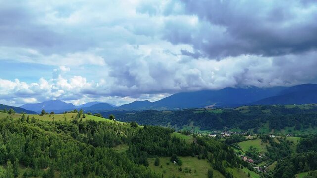 Aerial view of grassy hill at Pestera with Carpathians mountains peaks under the clouds