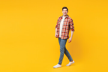 Fototapeta premium Full body side view young smiling cheerful happy man he wears red checkered shirt casual clothes walk go looking camera isolated on plain yellow orange background studio portrait. Lifestyle concept.