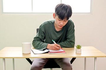 Young Asian Male Student Focusing On His Homework, Taking Notes or Making Lists On A Book.