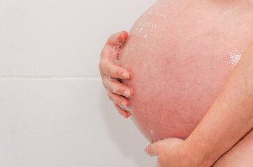Belly of a young pregnant woman while taking a shower in the bathroom. Future mother, happy...