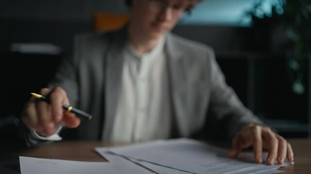 Close-up a confident young guy with curly hair in a gray jacket examines documents and signs while sitting at a table in the office