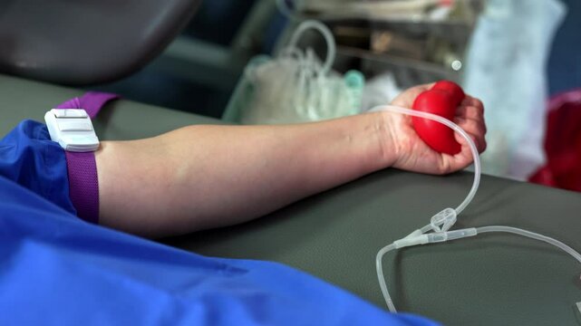 Donor's hand is squeezing the red rubber ball for blood inflow. Medic sprays the arm with antiseptic. Close up.