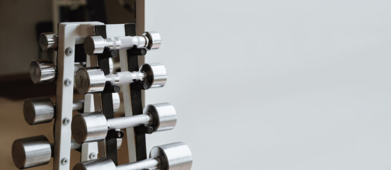 Dumbbell Rack in Fitness Gym close-up. Set of steel dumbbells of different weight. Business card with copy space on gray background. Sporting equipment for strong muscles. Sport shop. Club membership