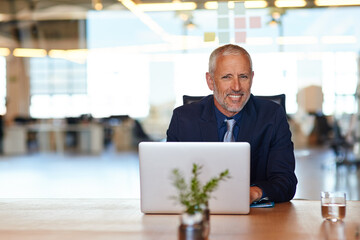 Laptop, portrait and smile of mature manager at desk in office for administration or research....