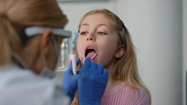Pediatrician taking child swab test in clinic closeup. Cute child opening mouth
