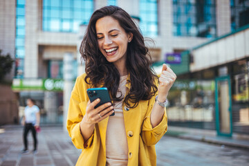 Happy Woman Celebrating Success While Using Smartphone Outdoors