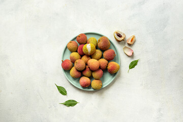 Juicy fresh lychee fruit with cut in half and green leaves on the plate, top view
