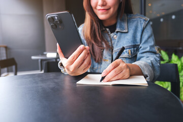 Closeup image of a woman writing on a notebook while using smart phone