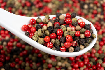 Different varieties of peppercorns, red, green, black and white peppers in a spoon