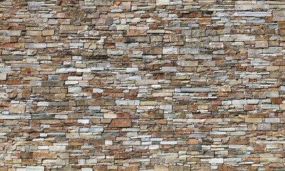 Large stone coating wall made of striped stacked bricks of natural multicolored rocks. Background and texture.