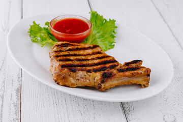Grilled pork chop resting on white plate with lettuce and tomato sauce