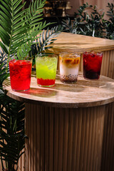 Four colorful summer cocktails resting on a stone tabletop in a tropical setting