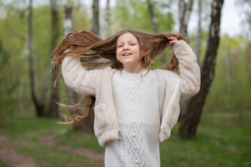 A beautiful girl with long hair in a fur coat poses against the background of a birch grove.