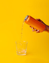 Woman pouring orange drink from can into glass on yellow background