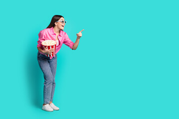 Full size photo of attractive teen woman watch movie point look empty space dressed stylish pink clothes cyan on blue color background