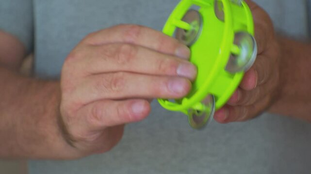 Hobbies and entertainment. Hands of an adult man playing a small plastic tambourine. Close-up. Shallow depth of field.