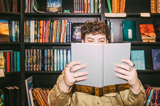 Young man reading book near shelf in bookstore