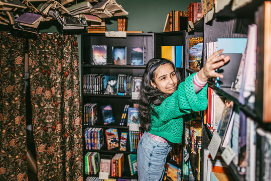Girl reaching for books arranged on shelf in bookstore