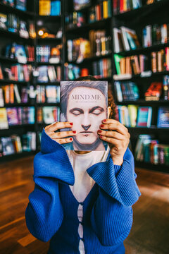 Young woman hiding face with book in bookstore