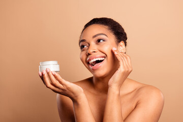 Photo of lovely pretty girl hold cream jar look empty space open shoulders isolated on beige pastel color background