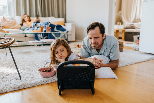 Father and daughter watching tablet PC lying down in living room at home