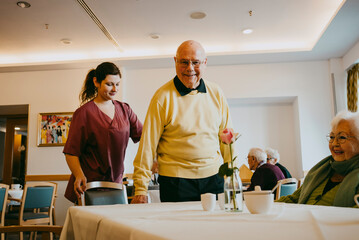 Female caregiver assisting senior man sitting at table in nursing home