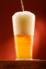 pouring beer into glass, wooden stand, red background, close-up view of object, beer foams and bubbles