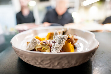 A close-up of a gourmet dish in a bowl, featuring textured food with a blurred background of people. Ideal for culinary, dining, and lifestyle themes. High-quality, appetizing presentation