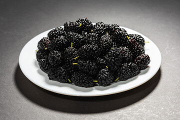 Fresh black mulberry on white plate on dark background. Concept of juicy and healthy seasonal...