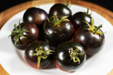 Ripe tomatoes in a white plate on a black background. Black tomatoes. Cumato tomatoes